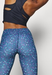 Leggings blu con motivo geometrico in rosa, viola e turchese. Tessuto leggero ed elastico con vita alta e cuciture piatte.