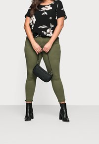 Svart blommig blus med korta ärmar, olivgröna skinny jeans och svarta ankelstövlar. Liten svart handväska med handledsrem.