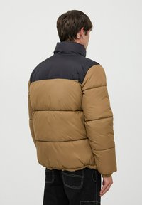 Giacca imbottita marrone e nera con colletto alto, design trapuntato, polsini e orlo elastici. Tessuto liscio, leggero e taglio moderno.