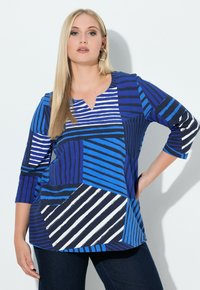 Blauw topje met verschillende geometrische vormen, met strepen in blauw, marineblauw en wit. V-hals ontwerp en driekwart mouwen.