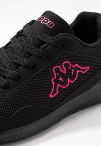 Svart sneakers med mesh- och mocka-textur, rosa Kappa-logotyp broderad på sidan, svarta snören och rosa Kappa-text på tungan.
