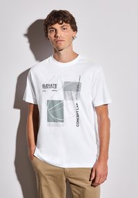 Bílý bavlněný tričko s abstraktním grafickým designem v šedé a zelené barvě s textem. Kulatý výstřih, krátké rukávy a volný střih.