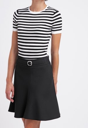 Vrouw die een zwart-wit horizontaal gestreept T-shirt met korte mouwen draagt, ingestopt in een zwarte A-lijn rok met gesp.
