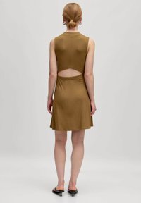 Ärmelloses braunes Kleid mit taillierter Oberseite und ausgestelltem Rock. Verfügt über einen ausgeschnittenen Rücken und einen strukturierten Stoff. Abgerundet mit schwarzen hohen Sandalen.