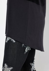 Top negro de manga corta con un dobladillo curvo, combinado con unos jeans negros desgastados que tienen parches en forma de estrella y bordes deshilachados.
