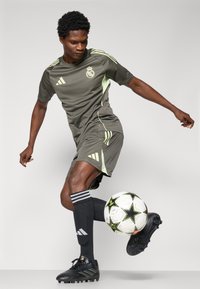 Grå fotballdrakt med grønne detaljer, med kort erm og striper, kombinert med svarte fotballsko og knelange svarte strømper. Sort-hvitt fotball.