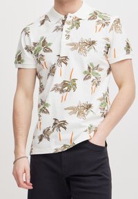 Witte polo met korte mouwen, versierd met een palmbomenpatroon in groen, bruin en oranje, met een klassieke kraag en een rechte zoom.