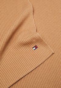 Tissu tricoté côtelé couleur chameau avec un petit logo brodé en rouge, blanc et bleu au bord inférieur.