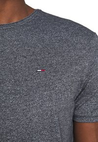 Korte mouwen shirt in donkergrijs, gemaakt van textuurstof. Heeft een klein geborduurd logo in rood, wit en blauw op de borst.