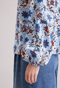 Blusa a stampa floreale caratterizzata da colori blu, rosso e bianco. Realizzata in tessuto morbido con polsini elasticizzati e una vestibilità ampia.