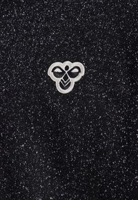 Stickat svart tyg med en prickig textur, med en vit broderad bi-logotyp. Designen innehåller subtila glittrande detaljer över hela ytan.