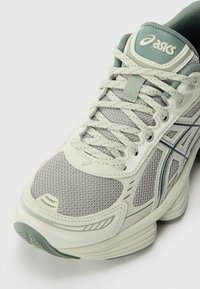 Shoe atlético cinza claro com parte superior em malha, detalhes verdes e sola texturizada. Apresenta atacadores, logotipo e design em camadas.