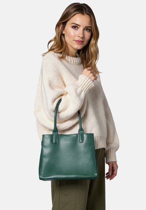 Borsa tote verde in pelle con due manici, forma rettangolare, texture liscia, ideale per uso casual o professionale. Il modello indossa un maglione crema.