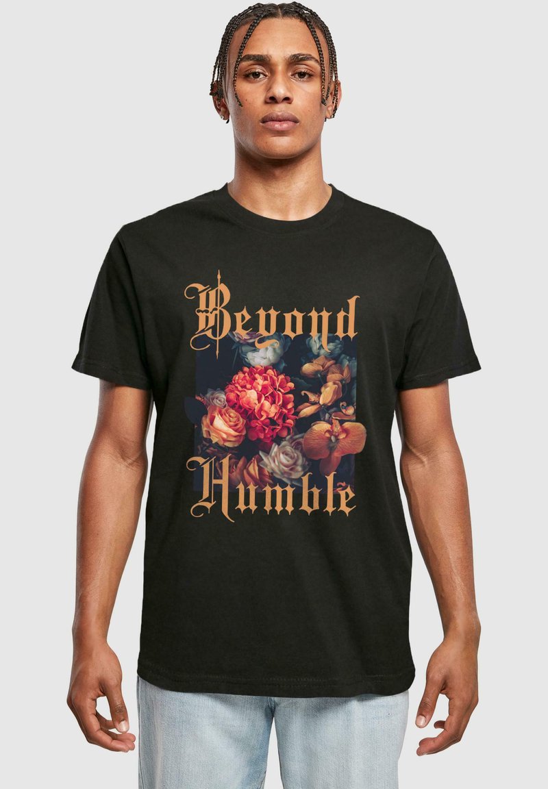 Sort bomulds t-shirt med et blomstermønster i klare farver og guldskrift, der siger "Beyond Humble." Enkel crew neck design.