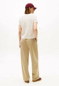 Beige bredde-bukser og en lys grå t-shirt, set bagfra, parret med en maroon kasket. Glat stof uden synlige mønstre.