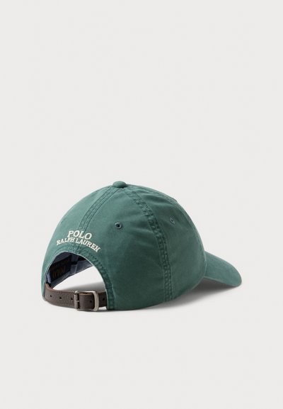 Tumši zaļa kokvilnas beisbola cepure ar izliektu vizieri, regulējamu brūnu ādas siksniņu un baltu izšūtu "Polo Ralph Lauren" logotipu aizmugurē.