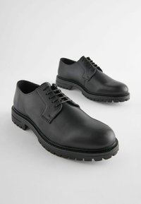 Zapatos de cuero negro de cordones con punta redonda, suela con patrón y detalles de costura en contraste. Diseño plano y duradero para mayor estabilidad.