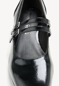 Chaussure Mary Jane en cuir verni noir avec brides à doubles boucles et semelle intérieure rembourrée.