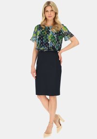 Bluzka w kwiaty w kolorze granatowym z zielonymi akcentami, zestawiona z dopasowaną granatową spódnicą ołówkową i beżowymi szpilkami. Elegancki design z miękkimi teksturami.