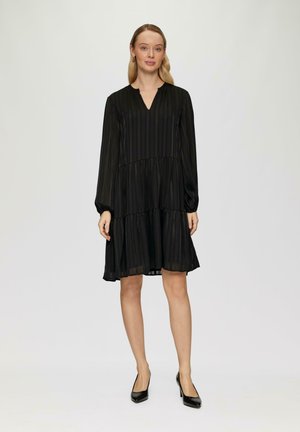 Robe noire à volants avec manches longues, décolleté en V et rayures verticales. Tissu léger et fluide avec un éclat subtil, associée à des talons noirs.