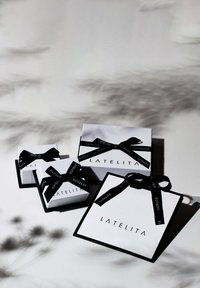Scatole regalo bianche con fiocchi di nastro nero etichettate "LATELITA", di diverse dimensioni, con un design elegante e angoli acuti, posizionate su uno sfondo chiaro.