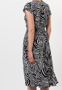 Vestido de patrón de cebra en blanco y negro con mangas cortas, cintura fruncida y falda fluida. El tejido parece ligero y con textura.