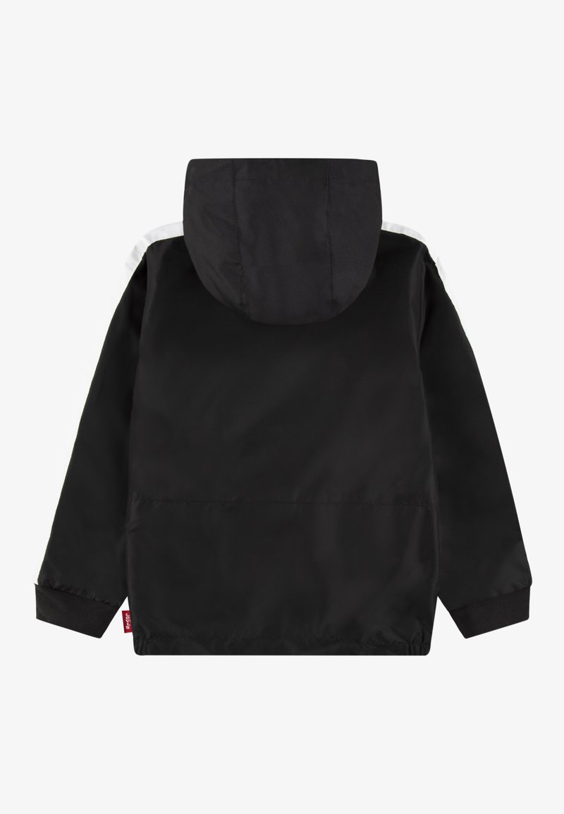 Schwarze Kapuzenjacke mit weißen Streifen auf den Schultern, langen Ärmeln, elastischen Bündchen und einem kleinen roten Stoffetikett an der unteren Seitennaht.