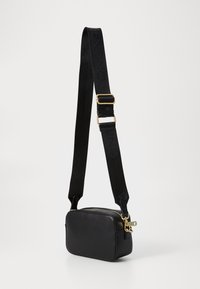 Sac à bandoulière rectangulaire noir en cuir lisse, avec une fermeture éclair dorée et une large sangle réglable texturée avec des détails de logo.