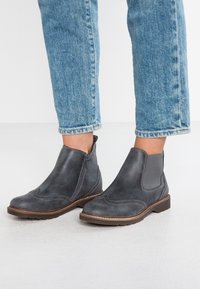 Šedé kožené kotníkové boty s elastickými bočními panely, dekorativním prošíváním a bočním zipem. Gumová podrážka s strukturovaným vzorem.