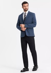 Niebieska marynarka z dwoma przednimi kieszeniami i dopasowanymi spodniami; biała koszula i czarna krawat w paski; czarne buty; gładkie faktury i dopasowany krój.