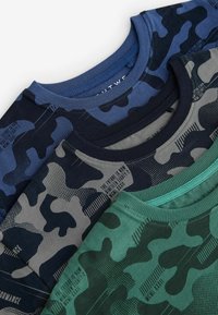 Tre crewneck T-shirts i olika färger: mörkblå, grå och grön kamouflage. Tillverkade av tyg med olika texturer och tryckdetaljer.