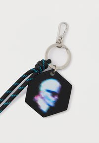 Εξαγωνικό μπρελόκ με ματ μαύρο φινίρισμα, διαθέτει στυλιζαρισμένο γραφικό. Περιλαμβάνει θηλιά και υφαντό κορδόνι σε μαύρο και μπλε. Μεταλλικό κλιπ για στερέωση.