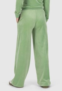 Pantalons larges en velours vert avec une taille élastique et des poches latérales, présentant une texture douce et une coupe décontractée.