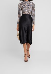 Svart satängkjol med en slät struktur, ihopparad med en mönstrad långärmad topp med guld- och blåmönster. Slinky svarta klackar.