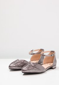Ballerines gris métallisé avec un bout pointu et un détail froncé. Dotées d'une bride à la cheville avec boucle et d'un talon bas et solide. Texture semblable au cuir.