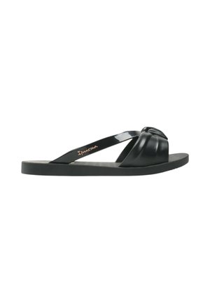 Sandalo nero piatto con cinturino superiore trapuntato e cinturino diagonale sottile con etichetta "Ipanema" su sfondo bianco.