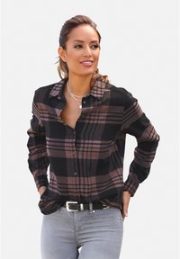 Crna i ružičasta karirana košulja s dugmadi, dugim rukavima i ovratnikom. Nošena je neuredno preko svijetlosivih traperica i crnog remena.