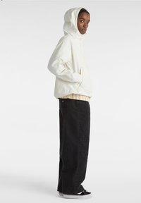 Letvægts, hættejakke i creme med en struktureret overflade, parret med oversized sorte jeans og afslappede sorte sko med hvide såler.