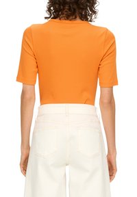 Pomarańczowa bluzka na krótki rękaw ma dopasowany krój. Zestawiona z wysokim stanem, jasnymi dżinsami z podwójnymi tylnymi kieszeniami i minimalnymi przeszyciami.