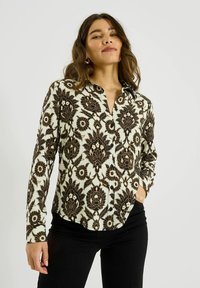 Camisa de manga larga con botones que presenta un patrón floral negro sobre un fondo marfil, hecha de una tela suave, con cuello y cierre de botones.