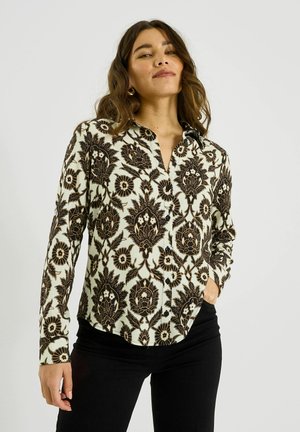 Camisa de manga larga con botones que presenta un patrón floral negro sobre un fondo marfil, hecha de una tela suave, con cuello y cierre de botones.