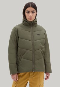 Chaqueta acolchada verde oliva con cuello alto, cierre de cremallera, textura acolchada y logotipo negro en el lado izquierdo del pecho. Indicado para uso en nieve o invierno.