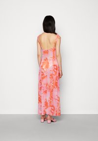 Vestido longo, sem mangas, em rosa, com padrões florais e laços ajustáveis nos ombros. O tecido suave cria uma silhueta fluida.