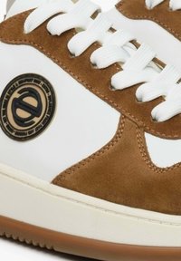 Białe sneakersy z brązowymi akcentami z zamszu, z okrągłą łatką z logo, białymi sznurówkami i teksturowaną podeszwą gumową.