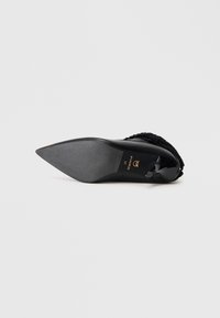 Zapato de tacón alto negro con punta afilada, parte superior texturizada y suela suave. Presenta un logo dorado y un diseño elegante. Talla 37.