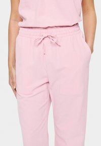 Light pink lounge pants with an elastic waistband, adjustable drawstring, and side pockets, made from soft, textured fabric.