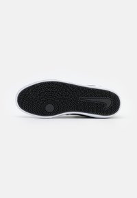 Sort gummisneakersål med zigzag mønster og hvid mellemsål; har cirkulært trækningspunkt og Nike-logo på siden.