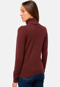 Pull à col roulé bordeaux avec des manches longues, un col côtelé, une texture douce, une coupe slim et un ourlet droit. Associé à un jean bleu foncé.