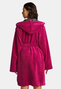 Fuchsiakleurige badjas met capuchon, gemaakt van zacht, pluizig materiaal, met een ceintuur in de taille en brede mouwen. Effen kleur zonder zichtbare patronen.