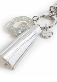 Portachiavi con una lettera "Q" trasparente e luccicante e un pompon in pelle bianca, con accessori in argento e un'etichetta circolare impressa con "MIRIADA."